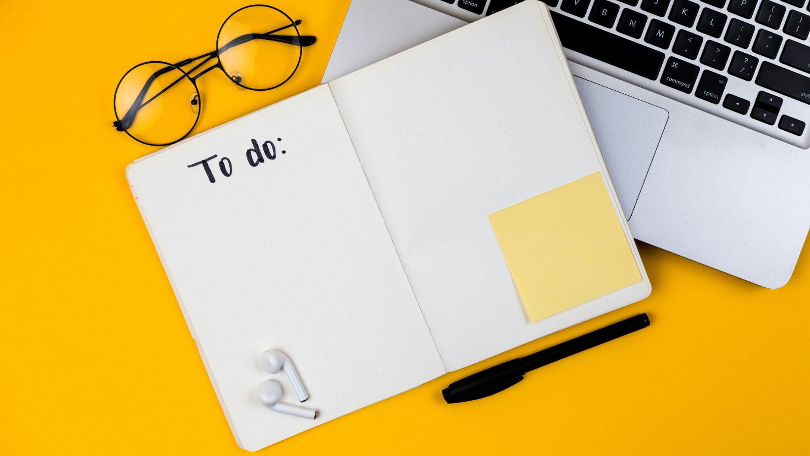 Planner, laptop, and glasses on a yellow surface