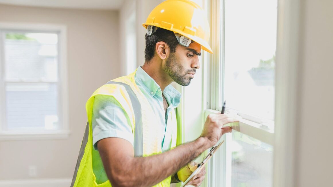 A man in a yellow vest inspecting a window